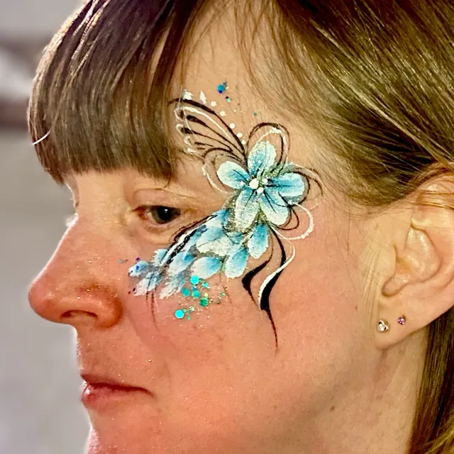 Blue flower and feather-style face painting with white and black swirls