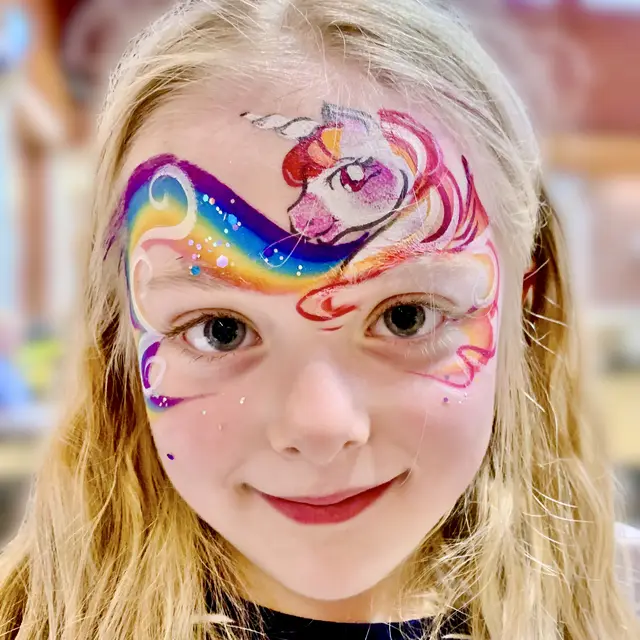 Rainbow unicorn face painting with pink swirls