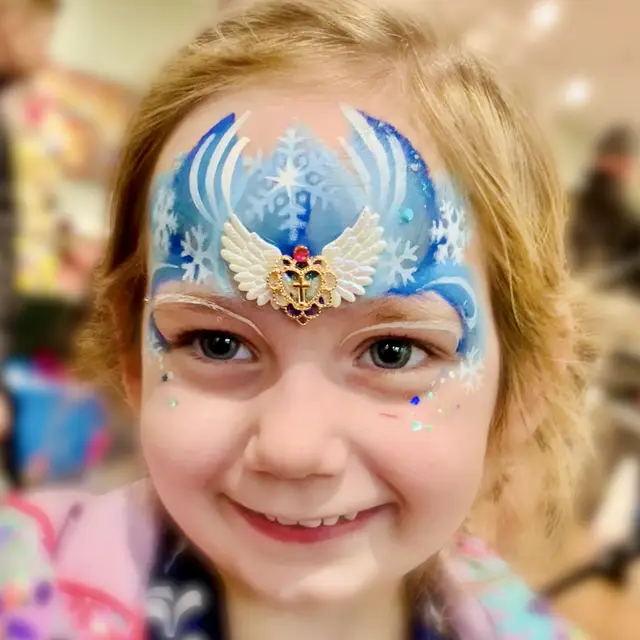 Blue snowflake face painting with a winged forehead jewel