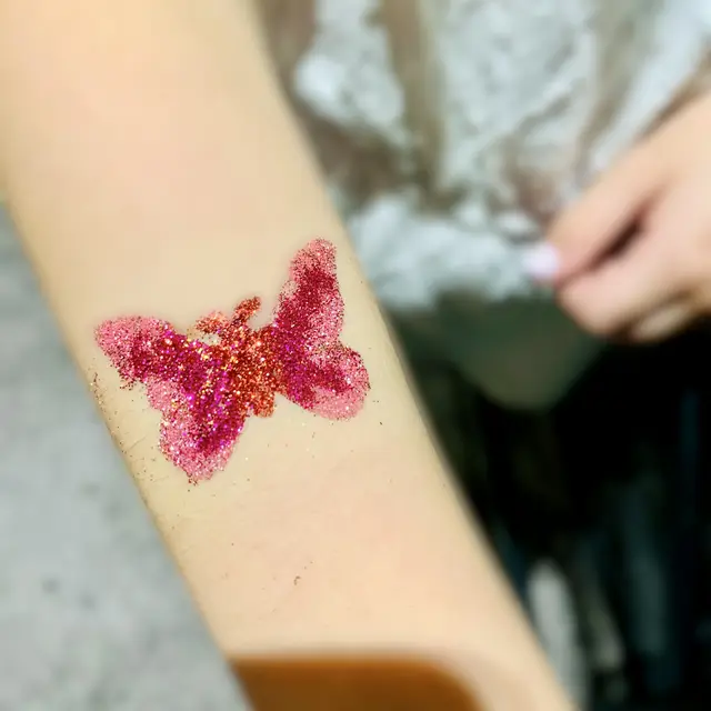 Pink glitter butterfly tattoo on an arm