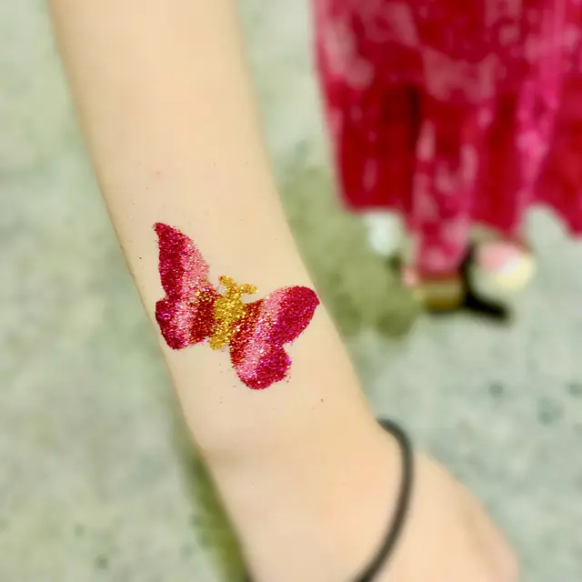 Two pink glitter butterfly tattoos on an arm